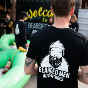 Man wearing black t shirt with bearded men adventures logo in white.
