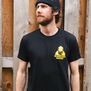 Man wearing black t shirt with yellow bearded men adventures logo and black beanie.